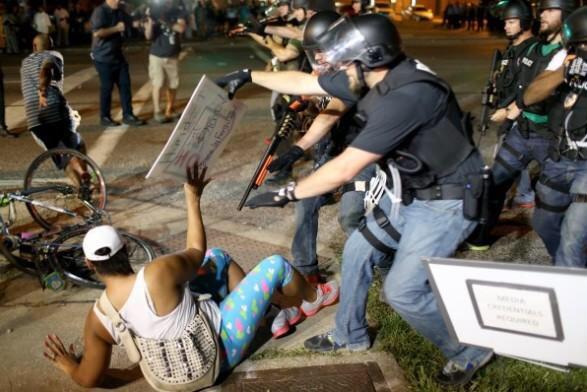 This protestor was holding a sign. Police respond with a shotgun in her face.