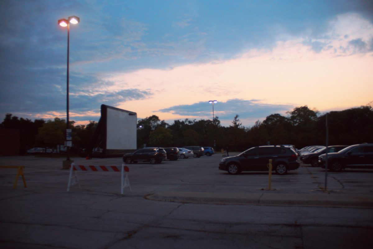 Cars are lined up for NEIU Alumni Association's Drive In Movie, with orange and white blocking dividers around area.   