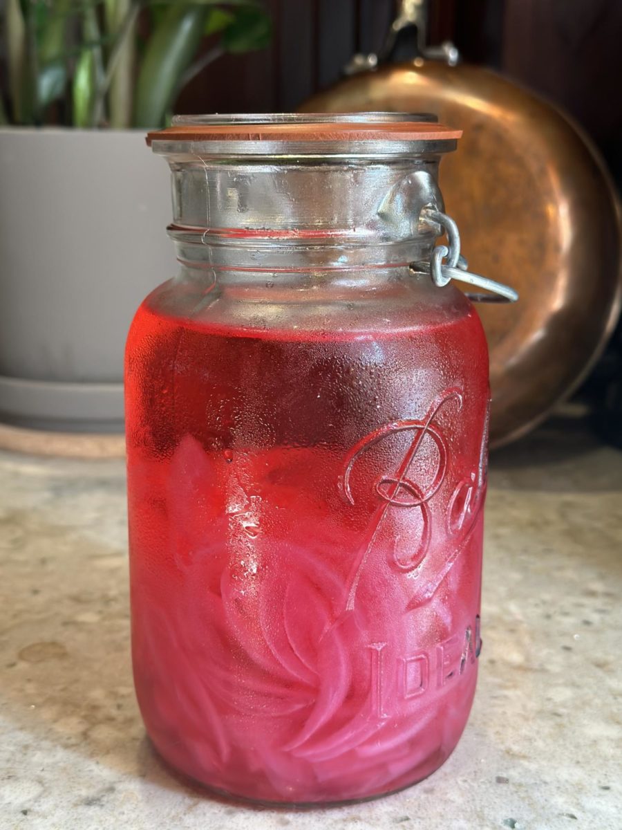 Picture of pickled red onions, in a glass jar, sitting on a counter.