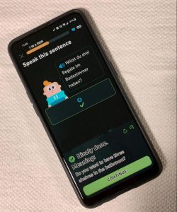 A photograph of a phone is displayed with single exercise of a lesson on the Duolingo app