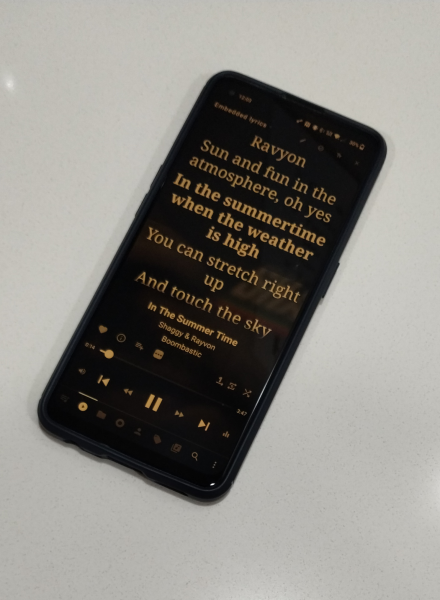 An Android phone has the Musicolet app playing the song "In The Summer Time" by Shaggy & Rayvon from the album "Boombastic." The synced lyrics are on screen, and the current lyric is in bolded font and reads, "In the summertime when the weather is high." Several controls of the music playing app are visible onscreen as well as several organizational icons along the bottom tray of the app.