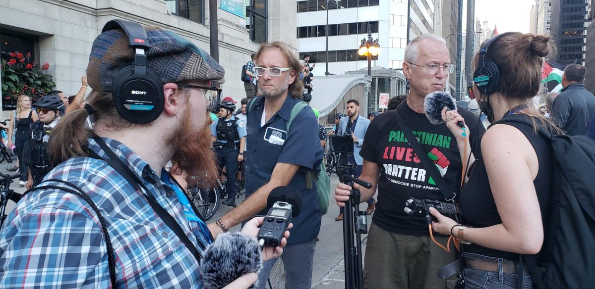 Dan Mauer (Left, flannel), News Editor, recording an interview with Dennis Sagel (Middle, white glasses), SMB Advisor, walks past.