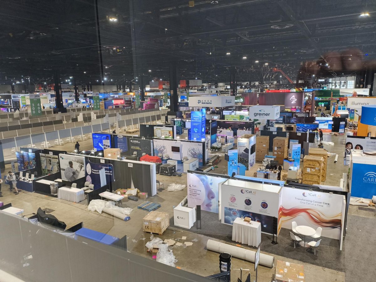 An overview of the AACR exhibitors’ booths is visible from the fourth-floor viewing area adjacent to the Grand Concourse of McCormick Place. The booths are still being set up prior to the first day of the conference, and carpets have yet to be unrolled in the aisles.