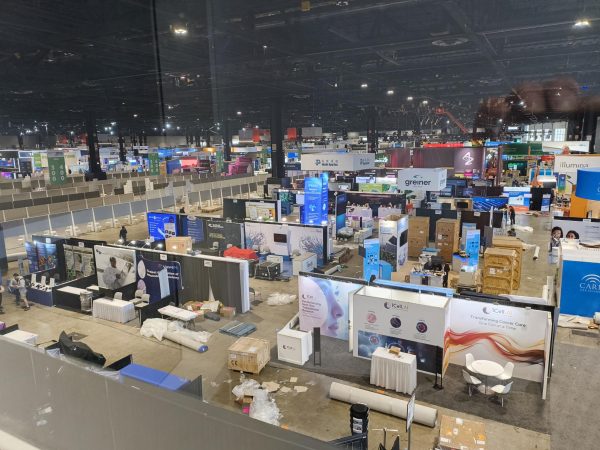 An overview of the AACR exhibitors’ booths is visible from the fourth-floor viewing area adjacent to the Grand Concourse of McCormick Place. The booths are still being set up prior to the first day of the conference, and carpets have yet to be unrolled in the aisles.